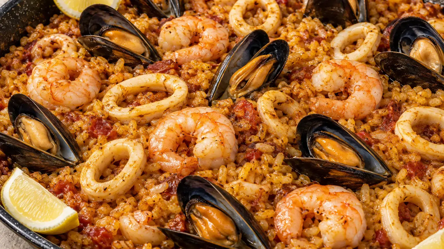 Paella with saffron rice, peeled shrimp, squid rings, mussels in their shells, and lemon