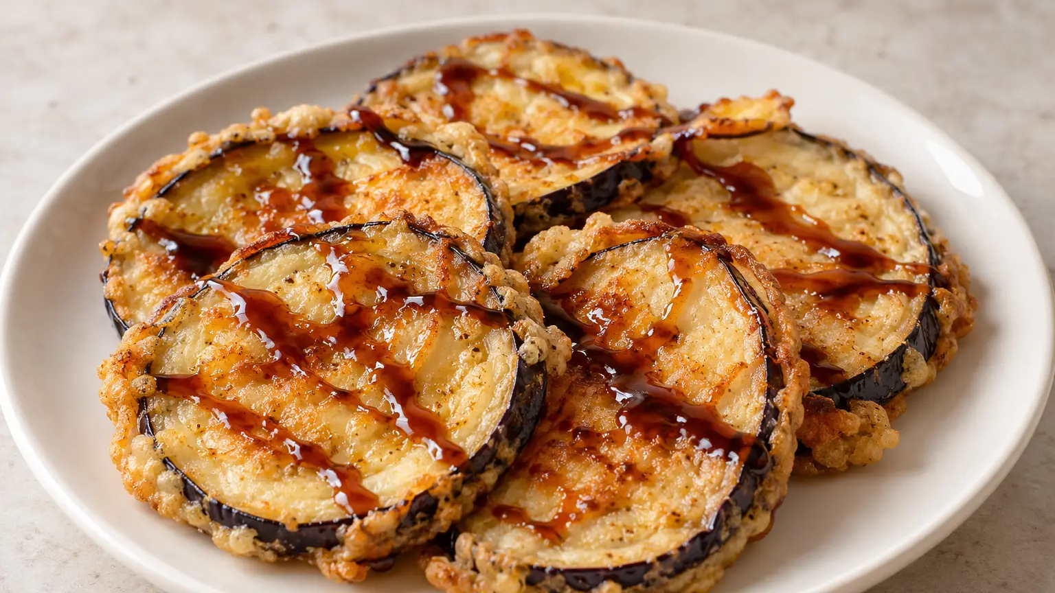 Golden eggplant slices with a thin crisp coating and dark cane syrup drizzles on a plate