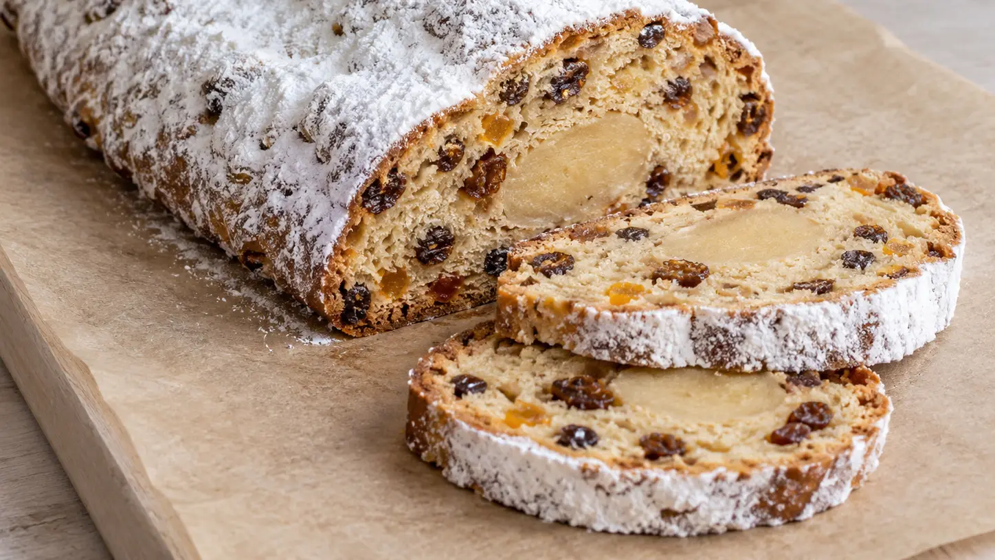 Langwerpige witte stollen met afgesneden plakken vol rozijnen en een lichte rol marsepein