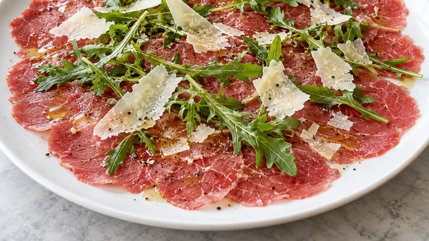 Carpaccio van dunne plakjes rauwe ossenhaas met rucola, Parmezaanschaafsel en olijfolie met citroen