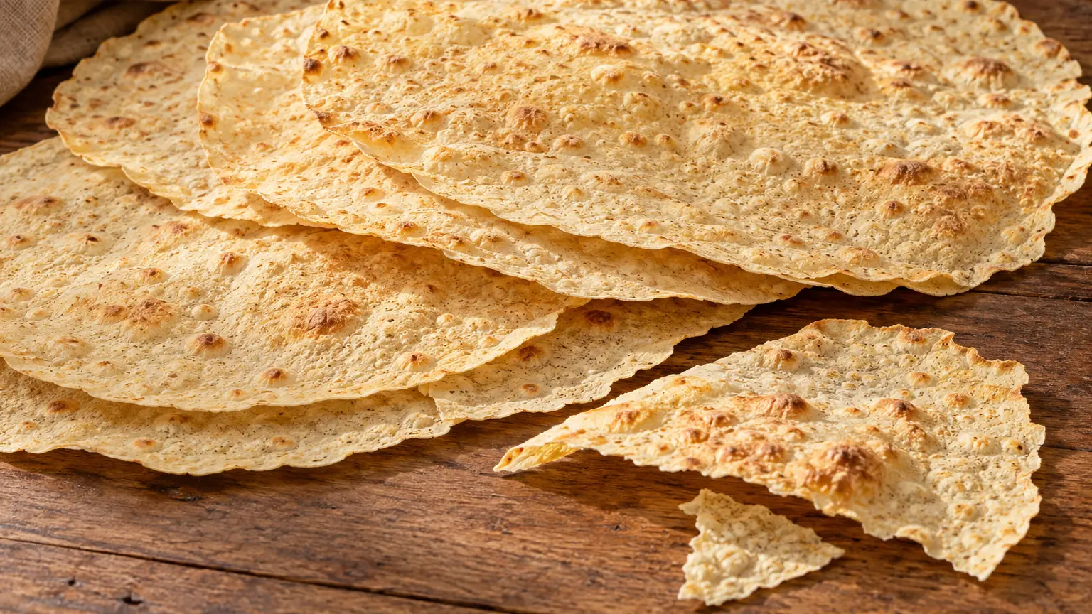 Sfoglie sottili leggermente dorate di pane carasau con frammenti croccanti su un piano semplice senza aggiunte